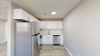 This 2-bedroom, 1-bathroom unit offers a clean, modern aesthetic across a single floor with a well-considered layout. Light-toned hardwood-style flooring runs throughout all rooms, lending a cohesive and contemporary feel to the space.

The living room is bright and open, featuring recessed lighting and a window with natural light, along with a wall-mounted HVAC unit and baseboard heating for year-round comfort. The kitchen is efficiently designed with white shaker-style cabinetry, a white subway tile backsplash, light stone countertops, and stainless steel appliances including a refrigerator, gas range, and dishwasher. Recessed lighting overhead keeps the space bright and functional.

The spacious primary bedroom is a standout, offering generous room for furnishings, multiple windows that invite natural light and outdoor views, and both baseboard heating and a wall HVAC unit. The second bedroom is also comfortably sized with a window and baseboard heating. Both bedrooms have access to dedicated closet storage.

The bathroom is neatly finished with large-format slate-toned tile flooring, a white vanity, and a tub-shower combination with tiled surround. A central hallway connects all rooms, creating a logical and easy-to-navigate flow throughout the unit.