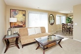 This single-floor residence offers a comfortable and functional layout designed for everyday living. The living room is bright and welcoming, featuring large vertical-blind-covered windows that flood the space with natural light, warm neutral walls, a textured ceiling, and plush carpeting underfoot. A glass-top coffee table and an open sightline to the dining area create a cohesive, connected feel throughout the main living space.

The dining area is situated adjacent to the kitchen and benefits from additional windows and a pendant light overhead, creating a cheerful atmosphere for meals. The kitchen is efficiently laid out in an L-shape, featuring white cabinetry, ample counter space, a double-basin sink, and a full suite of appliances including a range, microwave, dishwasher, and refrigerator, all set on durable tile flooring.

The primary bedroom is generously sized with soft carpeting and a window that brings in natural light. A secondary bedroom offers similar comfort and an equally cozy feel. Two bathrooms serve the residence — one with a shower-tub combination and overhead cabinetry, and an en-suite vanity area with a wide mirror and warm lighting. A dedicated in-unit laundry closet houses a full-size washer and dryer. A tiled entryway hallway with a closet completes this thoughtfully designed home.