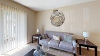 This single-floor residence offers a thoughtfully organized layout that balances comfort and functionality. The living room serves as the heart of the home, featuring plush carpeting, neutral warm-toned walls, and a large sliding glass door fitted with vertical blinds that floods the space with natural light and provides direct access to an outdoor area. The dining area is defined by warm hardwood-style flooring and anchored by a chandelier overhead, complemented by decorative wall art that adds a contemporary touch. The kitchen is efficiently designed with ample white cabinetry, generous counter space, and standard appliances including an electric range, providing a clean and practical cooking environment. The primary bedroom is a comfortable retreat with soft carpeting, a ceiling fan with integrated lighting, a window with curtains, and good natural light. The second bedroom mirrors this cozy feel, also featuring carpeted flooring, a ceiling fan, and a closet. The bathroom is bright and clean, appointed with white cabinetry, a well-lit vanity mirror, and hardwood-style flooring. Throughout the residence, a consistent palette of warm neutral tones and textured ceilings creates a cohesive and inviting ambiance.