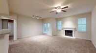 This 2-bedroom, 2-bathroom single-floor residence offers a thoughtfully designed layout across a generous footprint. The open living room serves as the heart of the home, featuring plush carpeting, a ceiling fan with light fixture, track lighting, and a classic wood-burning fireplace with a white mantel surround. French doors and multiple windows flood the space with natural light and provide outdoor views, while a pass-through opening connects seamlessly to the kitchen. The kitchen is well-equipped with rich, warm-toned cabinetry, light stone-finish countertops, wood-look flooring, and stainless steel appliances including a range and over-the-range microwave. A utility room is conveniently accessible from the kitchen. Both bedrooms are carpeted and include ceiling fans, with the primary bedroom offering a notably spacious layout and two windows with outdoor views. Each bedroom is served by a dedicated bathroom, both featuring wood-look tile flooring, a tub-shower combination, rich cabinetry, and brushed nickel hardware. Additional storage is provided by two closets, including one with a built-in wire shelving system. A hallway connects the private areas of the home, completing this functional and comfortable floor plan.