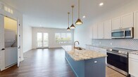 Located along the vibrant North High Street corridor in Columbus, Ohio, this single-floor unit offers a thoughtfully designed open-concept layout with modern finishes throughout. The kitchen serves as a true centerpiece, showcasing a bold teal island topped with granite countertops, a brushed gold faucet with an undermount sink, and three pendant lights with brass hardware suspended above. White shaker cabinetry lines the perimeter walls, complemented by a geometric diamond tile backsplash and stainless steel appliances, including a refrigerator, range, and microwave. Rich hardwood flooring extends throughout the main living and kitchen areas, anchoring the open plan. The living area is bathed in natural light from oversized windows and French doors that open to a private balcony with views of the surrounding neighborhood. Bedrooms feature plush carpet, decorative wall molding panels, and generous windows that bring in additional daylight. Each bathroom is finished with marble-look tile flooring, navy blue vanity cabinetry accented with gold hardware, white countertops, and subway tile surrounds in the shower and tub areas. Gold-toned sconces and framed mirrors complete the polished aesthetic. The overall design balances contemporary style with warm, inviting details throughout.