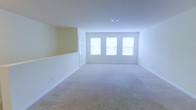 Located at 100 Reserve Ct in Grenville, New York, this single-floor residence offers a clean, well-maintained interior designed for comfortable everyday living. The main living area is a standout feature of the home, showcasing a spacious, open layout with plush wall-to-wall carpeting in warm neutral tones. Three large windows along the far wall flood the room with abundant natural light, creating a bright and airy atmosphere throughout the day. The walls are finished in a soft, neutral palette that complements the light carpeting and contributes to the overall sense of openness. A split-level architectural detail separates portions of the living space, adding visual interest and a subtle sense of definition without compromising the open feel. Smooth white ceilings with centrally placed ventilation keep the space feeling fresh and uncluttered. A doorway visible from the main living area provides easy access to additional rooms within the home. The overall design is straightforward and functional, offering a versatile canvas well-suited for a variety of furnishing styles and personal tastes. The single-floor layout ensures convenient, step-free living throughout the entire home.