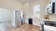 Located at 441 W Main St in Cary, Illinois, this two-bedroom, one-bathroom single-floor unit offers a thoughtfully designed layout with a clean, contemporary aesthetic. Warm-toned wood-look flooring flows consistently throughout the space, tying each room together cohesively.

The kitchen is a standout feature, showcasing tall ceilings that create an open, airy atmosphere. White shaker-style cabinetry with matte black hardware lines the walls, complemented by light countertops and a full suite of stainless steel and black appliances, including a French door refrigerator, gas range, over-the-range microwave, and dishwasher. A window above the sink fills the kitchen with natural light and views of the surrounding neighborhood.

The dining room impresses with soaring ceilings and a striking multi-arm candelabra-style chandelier as its centerpiece. A tall window allows generous natural light, enhancing the sense of volume in the space.

Both bedrooms are bright and well-proportioned, each featuring windows with blinds that bring in natural light and views of the outdoors. The primary bedroom offers a comfortable footprint suitable for standard furnishings.

The bathroom is clean and functional, featuring tile flooring, a wall-mounted sink, toilet with accessibility grab bars, and a tall storage cabinet, reflecting a practical and accessible design approach.