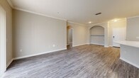 This single-story, 3-bedroom, 2-bathroom home offers a thoughtfully designed layout that balances comfort and functionality. The open-concept kitchen and living area serves as the heart of the home, featuring wood-look vinyl plank flooring, crisp white cabinetry with sleek hardware, a subway tile backsplash, light-toned countertops, and a peninsula with a built-in sink — ideal for both cooking and casual dining. Black appliances, including a refrigerator, range, microwave, and dishwasher, provide a sharp contrast to the bright cabinetry. The spacious living room is highlighted by elegant crown molding, decorative arched doorways, and a built-in shelving niche, creating a warm and refined atmosphere. The generously sized primary bedroom offers ample room to furnish comfortably. The additional bedrooms feature plush carpeting and natural light from window blinds. Both bathrooms are finished with tile flooring, white vanity cabinetry, and tub-shower combinations with classic tile surrounds. A dedicated laundry room accommodates a full-size washer and dryer side by side, complete with overhead shelving. The home's neutral color palette and consistent finishes throughout create a clean, cohesive aesthetic.