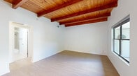 This single-floor residence showcases a distinctive architectural character defined by warm, rich wood beam ceilings with tongue-and-groove planking that span the main living areas, creating a welcoming and rustic-modern ambiance throughout. Light hardwood flooring runs consistently across the space, complementing the clean white walls and contributing to a bright, airy feel.

The kitchen is well-appointed with warm-toned wood cabinetry, stainless steel appliances including a French door refrigerator, built-in microwave, dishwasher, and gas cooktop. A sleek stone-topped island anchors the space, while a large window above the sink frames a verdant outdoor view. An in-unit laundry area is conveniently tucked nearby.

The living areas are generously proportioned, benefiting from soaring beamed ceilings and large windows that invite abundant natural light. The rooms offer an open, versatile layout with direct access to additional spaces. Bedrooms are bright and well-sized, featuring light hardwood floors, modern frosted-glass sliding closet doors with built-in organization, and windows overlooking greenery outside.

The bathroom is finished with neutral beige tilework, a combined tub and shower with a glass enclosure, and a backlit vanity mirror, completing this well-designed and cohesive living space.