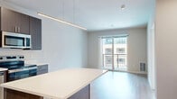 Located at 8421 Mansion Hill Ave in Madison, WI, this modern one-bedroom, one-bathroom unit offers a well-designed layout across a single floor. The open-concept kitchen and living area serves as the heart of the space, showcasing dark espresso cabinetry, light quartz countertops, a full suite of stainless steel appliances — including a refrigerator, electric range, microwave, and dishwasher — and a central island ideal for dining or meal prep. Recessed and pendant lighting illuminate the kitchen, while light-toned hardwood flooring runs throughout the main living areas, lending a clean, contemporary feel. The generously sized bedroom features plush carpeting, a large picture window that fills the room with natural light, a ceiling fan, and a sliding glass door that opens to a private balcony with exterior views. A dedicated closet provides convenient storage. The bathroom is finished with light wood-tone cabinetry and coordinates seamlessly with the unit's neutral palette. Crisp white Craftsman-style interior doors with matte black hardware add a refined architectural touch throughout. The overall ambiance is bright, modern, and move-in ready.