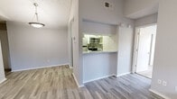This single-story residence offers a well-organized layout that balances open communal spaces with functional private areas. The living room serves as the heart of the home, highlighted by a brick fireplace, a ceiling fan with integrated lighting, and wood-look plank flooring in a cool gray tone. French doors allow natural light to pour in while providing a view of the outdoors. The kitchen is efficiently designed with white cabinetry, quartz-style countertops, a subway tile backsplash, and stainless steel appliances including a range and over-the-range microwave. A pass-through window connects the kitchen to the living area, enhancing the open feel. Adjacent to the kitchen, a louvered door conceals a stacked washer and dryer unit, offering in-unit laundry convenience. The bedroom is generously proportioned, finished with plush carpet, a ceiling fan, and multiple windows that bring in ample natural light and outdoor views. The bathroom features wood-look tile flooring, a mirrored vanity, and a dedicated closet space. Throughout the unit, neutral gray walls, textured ceilings, and consistent flooring create a cohesive and move-in ready aesthetic.