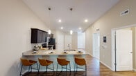 This single-floor residence at 3000 Twyckenham Blvd in Lafayette, Indiana, offers a thoughtfully designed layout with modern finishes throughout. The kitchen serves as a centerpiece of the home, showcasing dark espresso cabinetry, granite-style countertops, and a full suite of stainless steel appliances including a refrigerator, electric range, and over-the-range microwave. A generous island with an undermount sink provides seating for multiple guests and is illuminated by stylish pendant lighting. The living area features vaulted ceilings with a ceiling fan and rich hardwood-style flooring that flows through the main living spaces, creating a warm and cohesive ambiance. The bedrooms are carpeted for comfort, each featuring a ceiling fan with light fixture and windows with blinds that allow for natural light. Two bathrooms are finished consistently with wood-look vinyl flooring and dark vanity cabinetry topped with granite-style counters. One bathroom includes a tub/shower combination, while the other offers a stand-up shower. A hallway area provides access to multiple rooms and features recessed lighting and additional closet or storage doors. The neutral color palette and clean lines throughout give the home a fresh, move-in-ready appeal.