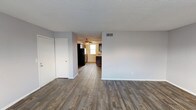 This single-floor unit offers a practical and comfortable layout across a well-utilized footprint. The living area is finished with durable wood-look plank flooring in a rich, dark tone, complemented by neutral gray walls and a textured ceiling throughout. A ceiling fan is positioned overhead, and a closet provides convenient storage directly within the living space. The open sightlines connect the living area to the kitchen, enhancing the sense of space.

The kitchen is equipped with dark espresso-toned cabinetry on both sides, granite-look countertops, a single-basin sink, and a window fitted with blinds that allows natural light to filter in. Black appliances, including a refrigerator, are visible from the main living area.

The bedroom features wall-to-wall carpet, soft gray walls, a window with blinds for natural light, and two doors—likely providing access to a closet and the hallway. The textured ceiling continues throughout this room.

The full bathroom includes a tub and shower combination with a curved curtain rod, chrome fixtures, and a toilet, offering a clean, functional design. Overall, the space presents a straightforward, move-in-ready layout with consistent finishes throughout.