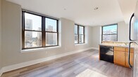 Located at 222 Market St in the heart of downtown Harrisburg, PA, this two-bedroom, one-bathroom residence offers a functional and well-appointed single-floor layout. The open-concept living and kitchen area is bright and airy, featuring light wood-style flooring that runs throughout. Large dark-framed windows frame sweeping views of the Harrisburg skyline, flooding the space with natural light.

The kitchen is well-equipped with warm wood cabinetry, granite-style countertops, a peninsula with bar seating, and a full suite of black appliances including a refrigerator, range, microwave, and dishwasher. The kitchen flows seamlessly into the living area, creating an inviting, connected space ideal for everyday living.

Both bedrooms are carpeted and comfortably sized, with the primary bedroom offering ample closet space and a city-facing window. The second bedroom also benefits from natural light. A hallway connects the main living areas to the bedrooms, providing a clear and practical layout.

The full bathroom features a granite-top wood vanity, a tub-shower combination, and wood-look tile flooring, maintaining a consistent, clean aesthetic throughout. Neutral wall tones and white trim give the entire unit a cohesive, modern feel.