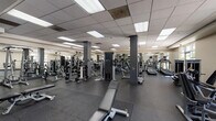 Located on Chandler Boulevard in North Hollywood, Los Angeles, this fitness center offers a comprehensive workout environment across a single, expansive floor. The facility is organized into distinct functional zones, allowing members to seamlessly transition between exercise types.

The cardio area is lined with treadmills, elliptical trainers, and other aerobic machines, each equipped with individual monitors for entertainment during workouts. Floor-to-ceiling mirrors along the walls amplify the sense of space and allow exercisers to monitor their form. The strength training section features a robust selection of cable machines, multi-functional weight stations, and adjustable benches suited for a wide variety of resistance exercises.

A dedicated free weights area provides a full dumbbell rack alongside additional benches, offering flexibility for targeted training. A water fountain station is conveniently accessible within this zone. The facility benefits from abundant natural light streaming through large glass doors and windows that open toward an outdoor area, complemented by recessed panel lighting in the drop ceiling throughout.

Durable rubber flooring covers the entire workout area, providing safety and comfort underfoot. Structural columns are integrated throughout the space, defining zones without impeding flow. The overall ambiance is clean, functional, and well-lit, making this fitness center a practical and fully equipped destination for a complete workout.