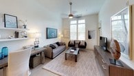 The Creek is a thoughtfully designed single-floor space that blends contemporary style with everyday functionality. The open-concept kitchen is a standout feature, showcasing crisp white cabinetry that extends to the ceiling for maximum storage, complemented by a charming gray tile backsplash that adds texture and depth. Stainless steel appliances — including a refrigerator, electric range, microwave, and dishwasher — offer a polished, modern aesthetic, while light hardwood-style flooring ties the space together seamlessly. The kitchen flows naturally into a dining area with a light stone-topped island, ideal for casual meals or entertaining.

The living room impresses with soaring ceilings and tall windows that invite abundant natural light, creating an airy, open atmosphere. A ceiling fan adds both style and comfort, while the neutral palette and light flooring lend the space a calm, contemporary feel.

The bathroom is clean and efficiently designed, featuring a full-size soaking tub with shower, a sleek white vanity with ample under-counter storage, brushed gold hardware accents, and large-format tile flooring. Warm, well-placed lighting over the vanity mirror completes the polished look. Throughout, the residence maintains a cohesive modern aesthetic defined by clean lines, neutral tones, and quality finishes.