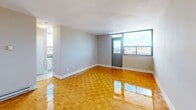 Located at 90 Tyndall Ave in Toronto's vibrant Parkdale neighbourhood, this efficiently designed unit offers a well-organized single-floor layout comprising a living area and a full bathroom. The living space is immediately distinguished by its polished parquet hardwood flooring, which adds warmth and classic character throughout. Neutral grey walls and white baseboards create a clean, bright backdrop, while large windows along one wall invite generous natural light and frame open city views of the surrounding Toronto skyline. A compact kitchen area is tucked to one side, making smart use of the available footprint. Built-in closet storage and a dedicated entryway add practical functionality to the layout. The bathroom is a standout feature, finished with large-format marble-effect wall tiles surrounding a full bathtub and shower combination, complemented by a small window that provides natural light. The overall ambiance is clean and understated, with a neutral palette that offers a versatile canvas. The unit's location in Parkdale places it within easy reach of transit, shops, and the eclectic dining and cultural amenities that define this established Toronto neighbourhood.