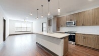 Located at 1400 Henderson Street in Fort Worth, Texas, this modern 2-bedroom, 2-bathroom residence offers a well-designed, single-floor layout with a thoughtful blend of style and functionality. The open-concept kitchen and living area serves as the heart of the home, featuring a large center island with a crisp white quartz countertop, warm wood-tone cabinetry extending to the ceiling, a white tile backsplash, and a full suite of stainless steel appliances including a range, microwave, and refrigerator. Sleek pendant lighting above the island adds a contemporary touch, while wood-style flooring flows throughout the main living areas. The living room is bright and airy, with wide windows dressed in horizontal blinds that invite natural light, complemented by a ceiling fan overhead. Both bedrooms are generously sized, each featuring ceiling fans and large windows. The primary bedroom offers hardwood-style flooring, while the secondary bedroom is finished with plush carpet. Each bathroom is well-appointed with dual-sink vanities, wood-tone cabinetry, white quartz countertops, glass-enclosed showers, and direct access to walk-in closets. A utility room and additional closet storage round out this well-organized and modern residence.