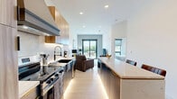 Located at 1923 Broadway Blvd in Kansas City, Missouri, this thoughtfully designed one-bedroom, one-bathroom unit offers a modern aesthetic with high-quality finishes throughout. The open-concept kitchen and living area serves as the heart of the space, where a striking quartz waterfall island with bar seating anchors the kitchen. Warm wood-grain upper cabinetry, a marble-style tile backsplash, under-cabinet lighting, and stainless steel appliances — including a smart refrigerator and a stainless range with a statement hood — complete the chef-inspired kitchen. Light hardwood flooring flows throughout the main living area, which is bathed in natural light from large sliding glass doors that open to a private balcony overlooking a tree-lined streetscape. The bedroom features plush carpet, a bright window with an outdoor view, and a dedicated closet with built-in shelving for organized storage. The bathroom impresses with large-format marble-look tile flooring, a dark wood vanity accented with gold hardware, and clean white countertops. Recessed lighting and a neutral color palette tie the entire space together, creating a polished, contemporary ambiance throughout.