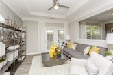 This thoughtfully designed single-floor residence offers a cohesive blend of modern finishes and functional layout. The kitchen features gray cabinetry, white appliances, and a peninsula with a clean white countertop that opens to the main living areas, all unified by warm wood-look luxury vinyl plank flooring. The living room is a standout space, highlighted by a tray ceiling with crown molding, a ceiling fan, and French doors that invite natural light and outdoor views. A built-in shelving unit adds both style and practicality to the room. The adjacent dining area is distinguished by wainscoting along the lower walls, large windows with outdoor views, and hardwood-style flooring that continues the cohesive aesthetic. Two well-sized bedrooms offer plush carpeting, generous natural light through large windows, and ample closet space — including a walk-in closet in the primary bedroom. The primary bathroom features a gray vanity with a white countertop, an undermount sink, and wood-look tile flooring. A second full bathroom is also present, finished with similar neutral tones. Throughout the residence, a consistent neutral color palette of warm grays and whites creates a calm, inviting ambiance.