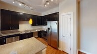 This single-floor residence offers a functional and cohesive layout with a neutral warm beige color palette throughout. The kitchen is a standout feature, showcasing dark espresso cabinetry extending to the ceiling, granite countertops, stainless steel appliances including a gas range and French door refrigerator, a peninsula for additional workspace, and track lighting accented by a pendant light. Hardwood-style flooring flows through the kitchen and main living area, where large windows and a ceiling fan bring in natural light and outdoor views.

The bedrooms are carpeted and each include ceiling fans with light fixtures, windows with blinds admitting generous natural light, and closet access. The primary bedroom features a tray ceiling detail, adding architectural interest. Two bathrooms serve the residence — one full bath with a tub/shower combination, hardwood-style floors, and a dark-cabinet vanity with chrome fixtures, and a second bath similarly finished with a backlit vanity mirror and clean white surfaces. A dedicated in-unit laundry area accommodates a full-size washer and dryer with an overhead wire storage shelf.