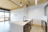 Located at 103 Virginia St in downtown Sioux City, Iowa, this urban loft offers a distinctive industrial-chic aesthetic that blends raw architectural elements with modern finishes. The open-concept layout seamlessly combines the living, dining, and kitchen areas into one cohesive, light-filled space. Soaring ceilings with exposed ductwork, piping, and wood-panel soffits lend an authentic loft character throughout. Polished concrete floors extend across the main living area, complementing the industrial feel.

The kitchen serves as a visual centerpiece, featuring a large island with sleek white quartz countertops, a double undermount sink, and a textured, mixed-material base. Dark espresso cabinetry — both upper and lower — pairs with a classic tile backsplash and a full suite of stainless steel appliances, including a refrigerator, range, and built-in microwave. Stylish pendant lighting above the island adds warmth and dimension.

The living area benefits from dramatic floor-to-ceiling windows that invite abundant natural light and offer open views of the surrounding cityscape. The bedroom is carpeted for comfort and includes access to multiple closets, providing generous storage. An in-unit laundry area adds everyday convenience. The space also features bold black door framing throughout, contributing to its modern, intentional design aesthetic.