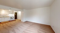 Located at 24440 Russel Rd in Kent, WA, this one-bedroom, one-bathroom unit offers a functional and comfortable single-floor layout. The open-concept main area seamlessly combines the living room, dining space, and kitchen, creating a versatile area well-suited for everyday living. The living room is carpeted and features a ceiling fan, vertical blinds allowing natural light, and baseboard heating. The kitchen is equipped with white cabinetry, a standard range, and a sink, with hard surface flooring that transitions from the adjacent carpeted areas. A hallway connects the main living space to the private bedroom and bathroom. The bedroom is generously sized, featuring plush carpet, vertical blinds over a window with outdoor views of greenery, and baseboard heating. Three closets throughout the unit provide ample storage. The bathroom is accessed via sliding frosted-glass doors and features white cabinetry, a granite-style countertop with an integrated sink, a mirrored vanity, and hard surface flooring. The unit's clean white walls and neutral color palette create a bright, airy atmosphere throughout, making it an efficient and practical living space.