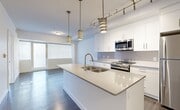 This well-appointed one-bedroom, one-bathroom unit at 10043 108 Street NW offers a thoughtfully designed layout that maximizes its compact footprint. A welcoming hallway with dark hardwood flooring leads into the open-concept kitchen and living area, which serves as the heart of the space. The modern kitchen features sleek white cabinetry, grey countertops, stainless steel appliances, and a central island with an integrated sink — all illuminated by stylish pendant lighting and a track lighting system overhead. The living area benefits from large windows that fill the space with natural light and provide views of the surrounding cityscape. The bedroom is a comfortable, well-lit room with hardwood-style flooring and large windows, accessed through a door that connects directly to a walk-in closet equipped with wire shelving for ample storage. The bathroom features a soaker tub with clean, white large-format tile surround, maintaining the unit's crisp, modern aesthetic. A dedicated laundry area adds everyday convenience. Throughout the unit, a consistent palette of white walls, light trim, and wood-tone flooring creates a cohesive, contemporary atmosphere that is both functional and visually appealing.