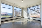 Located at 142 Paoli St in Verona, WI, this thoughtfully designed two-bedroom, one-bathroom single-floor residence offers a clean, modern aesthetic throughout. Polished concrete floors and crisp white walls create a cohesive, contemporary feel from room to room.

The open-concept kitchen is a standout feature, boasting warm honey-toned cabinetry, light stone countertops, stainless steel appliances including a refrigerator, range, and over-the-range microwave, and a peninsula with an integrated sink — illuminated by elegant pendant lighting that highlights the impressively tall ceilings above.

Both bedrooms are generously proportioned, each benefiting from oversized picture windows framed in dark metal that frame scenic views of mature trees and the surrounding natural landscape, flooding the rooms with abundant natural light. The primary bedroom offers a comfortable footprint well-suited for a full furniture arrangement.

The bathroom features a warm wood vanity with white countertop and a textured glass partition, maintaining the modern design language found throughout the home. A long, well-lit hallway connects the living spaces, and dedicated laundry, closet, and entrance areas add practical functionality. The overall ambiance is bright, airy, and distinctly modern.