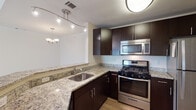 This two-floor residence offers a thoughtfully designed layout that balances modern finishes with comfortable living. The kitchen is a standout feature, equipped with rich dark cabinetry, granite countertops, a full suite of stainless steel appliances including a gas range, microwave, and refrigerator, and a peninsula that opens toward the dining area. Track lighting and a decorative chandelier illuminate the space effectively.

The living area commands immediate attention with its dramatic vaulted ceilings and an upper-level overlook connected by a wood-railed staircase. A fireplace serves as a focal point, while a sliding glass door with vertical blinds allows natural light to fill the room. Soft carpet underfoot adds warmth throughout the main living and bedroom areas.

The hallway connecting the bedrooms is clean and bright, lined with classic six-panel doors and neutral carpet. Bedrooms are generously sized, with windows fitted with slatted blinds and ceiling fan fixtures providing both light and ventilation. One bedroom features a tray ceiling detail for added architectural interest.

Both bathrooms are finished with granite-topped dark vanities and tile flooring. Each includes a shower-tub combination, offering functional and consistent design. The overall aesthetic is clean, neutral, and move-in ready.