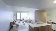 Located at 66 Summer Street in the heart of Stamford, Connecticut, this single-floor residence offers a thoughtfully designed open-concept layout that seamlessly connects the living, dining, and kitchen areas. The kitchen features a sleek, modern island with a clean white countertop and warm wood-toned cabinetry, providing both a functional workspace and a casual dining area with seating. The open living space is bathed in natural light from large windows that frame views of the surrounding cityscape, creating a bright and airy ambiance throughout. The living area offers generous room for comfortable seating arrangements, complemented by neutral tones and contemporary décor. The smooth white ceilings and clean wall finishes contribute to a minimalist aesthetic that enhances the sense of openness. The dining area flows naturally from the kitchen island, making the space ideal for both everyday living and entertaining. Overall, the residence presents a cohesive modern design with a light, welcoming atmosphere, well-suited to urban living in downtown Stamford.