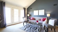 Located at 713 Willow Lake Cir in Virginia Beach, Virginia, this two-story home offers a well-designed layout across two levels. The living room is a standout space, featuring a dramatic vaulted ceiling with a bold accent wall and French doors that invite natural light and provide outdoor access. The adjacent dining area is brightened by multiple windows dressed with sheer curtains and is anchored by an overhead chandelier, creating an inviting atmosphere for everyday meals or gatherings. The kitchen is equipped with rich dark wood cabinetry, laminate countertops, tile flooring, and white appliances including a range and dishwasher. Bedrooms are carpeted and offer generous proportions, with accent walls adding a pop of color and character. The primary bedroom includes access to a private en-suite bathroom featuring a wood vanity, tile flooring, and a tub-shower combination. A second full bathroom mirrors this functional design. The upper level, accessible via a staircase with a railing, provides additional bedroom space with a textured ceiling and soft carpet. A dedicated utility and laundry room houses the water heater and washer, adding convenience. Throughout, the home maintains a clean, neutral palette with thoughtful accent colors and an easy-flowing floor plan.