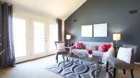 Located at 713 Willow Lake Cir in Virginia Beach, Virginia, this two-story home offers a well-designed layout across two levels. The living room is a standout space, featuring a dramatic vaulted ceiling with a bold accent wall and French doors that invite natural light and provide outdoor access. The adjacent dining area is brightened by multiple windows dressed with sheer curtains and is anchored by an overhead chandelier, creating an inviting atmosphere for everyday meals or gatherings. The kitchen is equipped with rich dark wood cabinetry, laminate countertops, tile flooring, and white appliances including a range and dishwasher. Bedrooms are carpeted and offer generous proportions, with accent walls adding a pop of color and character. The primary bedroom includes access to a private en-suite bathroom featuring a wood vanity, tile flooring, and a tub-shower combination. A second full bathroom mirrors this functional design. The upper level, accessible via a staircase with a railing, provides additional bedroom space with a textured ceiling and soft carpet. A dedicated utility and laundry room houses the water heater and washer, adding convenience. Throughout, the home maintains a clean, neutral palette with thoughtful accent colors and an easy-flowing floor plan.