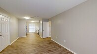 This single-floor 1-bedroom, 1-bathroom unit offers a clean, contemporary design throughout. The open living area is finished with warm hardwood-style vinyl flooring and neutral gray walls, creating a bright and welcoming atmosphere. Natural light flows in through multiple windows, enhancing the sense of space. French doors in the main living area provide outdoor access and fill the room with additional light.

The kitchen is well-appointed with white shaker-style cabinetry extending to the upper walls, light granite-look countertops, a double-basin sink, and black appliances including a refrigerator, range, and dishwasher. A centered window above the sink adds natural light to the cooking space.

The bedroom features plush carpeting and its own set of French doors, offering a private and comfortable retreat. The full bathroom includes a tub-shower combination with tile surround, a white vanity with granite-look countertops, a single-basin sink, and a large mirror above.

A hallway connects the main living spaces efficiently, with additional doors providing access to storage or utility areas. The consistent use of neutral tones, white trim, and coordinated finishes throughout the unit lends it a cohesive, move-in-ready aesthetic.