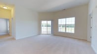 Located at 100 Isabelle Isle in Dover, Delaware, this single-floor home offers a clean, open layout designed to maximize comfort and natural light. The main living area is expansive and airy, finished with neutral wall-to-wall carpeting that adds warmth underfoot. Elevated ceilings enhance the sense of openness, creating a bright and welcoming atmosphere throughout. A set of sliding glass doors provides direct access to an outdoor area, while a large adjacent window frames lush greenery and open yard views, filling the room with abundant natural light. The neutral, light-toned walls complement the soft carpeting, offering a versatile backdrop suited to a variety of interior styles. The overall design is straightforward and functional, emphasizing open space and connectivity to the outdoors. The single-floor layout ensures seamless flow throughout the home, making it both practical and easy to navigate. This property combines understated architectural simplicity with bright, inviting interiors, making it an ideal space for those seeking a comfortable and well-lit living environment in Dover, Delaware.