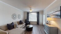 This single-story, 2-bedroom, 2-bathroom residence is thoughtfully laid out to maximize both comfort and functionality. The living room serves as the heart of the home, featuring rich hardwood-style flooring, crown molding, and a ceiling fan overhead. Natural light streams through a large arched window dressed with elegant drape panels, creating a bright and welcoming atmosphere. A partial wall with a decorative column subtly separates the living area from the dining space, adding architectural interest while maintaining an open feel. The kitchen is well-equipped with ample white cabinetry, generous counter space, and a full suite of appliances including a range, microwave, and dishwasher. A pass-through window connects the kitchen to the adjacent dining area for added convenience. Both bedrooms are carpeted and generously sized, each featuring ceiling fans and walk-in closets with built-in shelving. The primary bathroom includes a dual-sink vanity with a large mirror and hardwood-style flooring, while the second bathroom offers a shower-tub combination. Throughout the residence, a neutral color palette and clean finishes create a cohesive, inviting ambiance well-suited for everyday living.