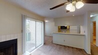This 1-bedroom, 1-bathroom apartment is thoughtfully laid out across a single floor, offering a comfortable and functional living environment. The open living area features soft carpeting, a ceiling fan with light fixture, and a textured ceiling. A standout feature is the tile-surround fireplace, adding warmth and character to the space. Sliding glass doors with vertical blinds lead to a private balcony, filling the room with natural light and outdoor views of surrounding greenery. The kitchen runs along a galley-style corridor and is equipped with white appliances including a range, refrigerator, and dishwasher, alongside a built-in microwave, ample cabinetry, and a peninsula counter that opens toward the living area. Light vinyl tile flooring runs through the kitchen. The bedroom is a well-proportioned room with plush carpeting, a ceiling fan, and a window that brings in natural light. The full bathroom includes a tub-shower combination, a wood-accented vanity with a wide mirror, and tile flooring. Throughout the unit, ceiling fans in each room provide efficient climate control, complementing the overall practical and comfortable design of the space.