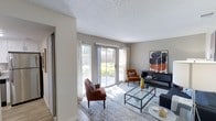 This single-floor space offers a welcoming and well-appointed interior designed with both comfort and style in mind. The living area serves as the heart of the home, bathed in natural light streaming through large sliding glass doors that open to an outdoor patio area, framing views of the surrounding greenery. The textured ceiling adds a classic architectural touch, while the neutral wall tones create a versatile backdrop that complements the warm, earthy furnishings throughout. The living room is thoughtfully arranged with rich terracotta-hued accent chairs, a sleek glass-top coffee table, and a bold abstract art piece that adds a contemporary flair to the space. Hardwood-style flooring runs throughout, topped with a soft area rug that anchors the seating arrangement. A dark console table provides additional display and storage space, while the abundant natural light enhances the airy, open feel of the room. The sliding glass doors not only flood the space with sunlight but also create a seamless connection between the indoor living area and the outdoor patio, making the space feel expansive and inviting. Overall, the space strikes a balance between modern aesthetics and comfortable livability.