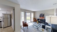 This single-floor space offers a welcoming and well-appointed interior designed with both comfort and style in mind. The living area serves as the heart of the home, bathed in natural light streaming through large sliding glass doors that open to an outdoor patio area, framing views of the surrounding greenery. The textured ceiling adds a classic architectural touch, while the neutral wall tones create a versatile backdrop that complements the warm, earthy furnishings throughout. The living room is thoughtfully arranged with rich terracotta-hued accent chairs, a sleek glass-top coffee table, and a bold abstract art piece that adds a contemporary flair to the space. Hardwood-style flooring runs throughout, topped with a soft area rug that anchors the seating arrangement. A dark console table provides additional display and storage space, while the abundant natural light enhances the airy, open feel of the room. The sliding glass doors not only flood the space with sunlight but also create a seamless connection between the indoor living area and the outdoor patio, making the space feel expansive and inviting. Overall, the space strikes a balance between modern aesthetics and comfortable livability.