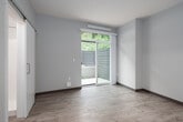This thoughtfully designed single-floor studio offers a clean, modern aesthetic with an efficient and functional layout. The main living area features light wood-tone flooring, neutral wall tones, and recessed lighting that creates a bright and welcoming atmosphere. A sliding glass door floods the space with natural light and provides direct access to a private outdoor patio enclosed by horizontal-slat privacy fencing, with lush greenery visible beyond — offering a serene outdoor retreat.

The kitchenette is well-appointed with warm natural wood upper cabinetry, a dark countertop with a stainless steel undermount sink and pull-down faucet, a compact refrigerator, and a built-in microwave, all set against a soft blue backsplash that adds a subtle pop of color. The efficient design maximizes storage while keeping the space open and uncluttered.

The bathroom is finished with a clean, minimalist design, featuring a wall-mounted sink, a mirrored medicine cabinet, and polished chrome fixtures and accessories including a towel ring and towel bar. The overall unit is characterized by its contemporary finishes, efficient use of space, and seamless indoor-outdoor connection, making it a practical and comfortable living environment.