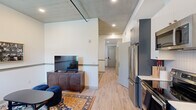 Located at 808 Constance St in New Orleans' historic Lower Garden District, this single-floor unit offers a well-appointed layout across four rooms, combining contemporary design elements with warm, inviting character. Exposed concrete ceilings lend an industrial-chic aesthetic throughout, complemented by light hardwood flooring that runs continuously and ties the space together seamlessly.

The open living and kitchen area forms the heart of the unit, where sleek gray cabinetry, stainless steel appliances, and white countertops create a modern, functional kitchen. The living area accommodates comfortable seating and entertainment, with recessed lighting illuminating the space. An elegant sitting nook features a large draped window that invites natural light, anchored by a classic upholstered loveseat and a decorative wall sconce.

The bedroom is a serene retreat, featuring a tufted velvet headboard, warm bedside lighting, curated wall art, and a round wood-framed mirror that adds depth to the room. A chair rail detail runs along the walls, adding architectural refinement throughout the unit.

The bathroom offers a polished finish with a glass-enclosed walk-in shower adorned with checkerboard tilework, brushed gold fixtures, and bold blue wainscoting that adds a distinctive pop of color. A private entry corridor with multiple doors ensures a clear separation between living areas, enhancing both functionality and flow.