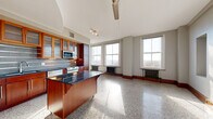 Located in the heart of downtown Tulsa at 427 S Boston Ave, this one-bedroom, one-bathroom unit blends historic character with modern updates. The open-concept living area combines the kitchen, dining, and living spaces into one expansive, sun-drenched room. Rows of large, tall windows line the exterior wall, flooding the polished terrazzo floors with natural light while offering views of the surrounding cityscape. Classic cast-iron radiators beneath the windows add a charming industrial touch that honors the building's historic roots.

The kitchen is well-appointed with rich warm-toned wood cabinetry featuring glass-front upper cabinets, dark granite countertops, a tile backsplash, and a full suite of stainless steel appliances including a range, microwave, and dishwasher. A movable kitchen island with a dark countertop provides additional workspace and flexibility. A ceiling fan anchors the living area, complementing the track lighting over the kitchen zone.

The generously sized primary bedroom offers ample space, while two closets provide substantial storage. A dedicated laundry area and hallway add further practicality. The bathroom continues the terrazzo flooring and includes a tiled tub-shower combination. Throughout the unit, clean white walls and warm wood trim create a cohesive, inviting aesthetic rooted in the character of this distinguished historic building.