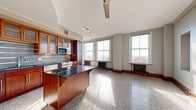 Located in the heart of downtown Tulsa at 427 S Boston Ave, this one-bedroom, one-bathroom unit blends historic character with modern updates. The open-concept living area combines the kitchen, dining, and living spaces into one expansive, sun-drenched room. Rows of large, tall windows line the exterior wall, flooding the polished terrazzo floors with natural light while offering views of the surrounding cityscape. Classic cast-iron radiators beneath the windows add a charming industrial touch that honors the building's historic roots.

The kitchen is well-appointed with rich warm-toned wood cabinetry featuring glass-front upper cabinets, dark granite countertops, a tile backsplash, and a full suite of stainless steel appliances including a range, microwave, and dishwasher. A movable kitchen island with a dark countertop provides additional workspace and flexibility. A ceiling fan anchors the living area, complementing the track lighting over the kitchen zone.

The generously sized primary bedroom offers ample space, while two closets provide substantial storage. A dedicated laundry area and hallway add further practicality. The bathroom continues the terrazzo flooring and includes a tiled tub-shower combination. Throughout the unit, clean white walls and warm wood trim create a cohesive, inviting aesthetic rooted in the character of this distinguished historic building.