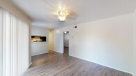 This single-floor unit offers a clean, modern aesthetic highlighted by durable hardwood-style flooring that runs consistently throughout the space. The open living area is bright and welcoming, featuring a ceiling fan with a light fixture and a sliding glass door fitted with vertical blinds that allows natural light to fill the room while providing access to an outdoor patio area. A pass-through connects the living area to the kitchen, which is thoughtfully designed with dark espresso cabinetry, granite-style countertops, a stainless steel double-basin sink, and a dishwasher — offering both functionality and style. Each bedroom is comfortably proportioned with its own ceiling fan, neutral-toned walls, and the same hardwood-style flooring, creating a cohesive feel across the unit. The bathroom features a dark-framed vanity mirror, a wide granite-topped countertop with ample storage below, and a full bathtub with white tile surround. A dark upper cabinet above the toilet provides additional storage. Throughout the unit, clean white walls, consistent trim, and updated finishes contribute to a fresh and well-maintained atmosphere.