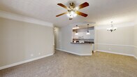 Located at 800 Gunn Rd in Centerville, Georgia, this single-story home offers a well-designed layout with a cohesive, neutral color palette that creates a warm and inviting atmosphere throughout. The spacious living room serves as the heart of the home, featuring plush carpeting, crown molding, a textured ceiling, and a ceiling fan with light fixture. An arched pass-through opening connects the living area to the kitchen, which is equipped with white cabinetry, dark laminate countertops, a double basin sink, and white appliances including a refrigerator, electric range, and built-in microwave. Wood-look flooring runs through the kitchen, adding a clean contrast to the carpeted living spaces. A breakfast bar with pendant lighting bridges the kitchen and living area, while a chandelier-lit dining space sits adjacent. The primary bedroom is generously sized with large windows that invite natural light, carpet flooring, crown molding, and direct access to a walk-in closet and a private en-suite bathroom. Additional bedrooms are well-proportioned with ceiling fans and closet access. Bathrooms feature tub-shower combinations, white vanities, and wood-look flooring accented with gold hardware. The floor plan flows efficiently, making this home both functional and comfortable.