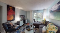 This single-floor residence offers a well-organized layout designed for comfortable everyday living. The living room serves as the heart of the home, featuring soft blue-gray walls, light wood-style flooring, and a large window that fills the space with natural light and offers a view of lush greenery outside. A sectional sofa, glass-top coffee table, and a bold, vibrant area rug give the room a contemporary and inviting character.

The galley-style kitchen is both functional and stylish, outfitted with dark gray cabinetry, white countertops, wood-look flooring, and black appliances, creating a sleek modern aesthetic.

The bedrooms are carpeted and thoughtfully appointed. One bedroom features warm yellow walls and a large window overlooking outdoor greenery, while another showcases a calming teal accent wall with decorative wall art and direct access to a hallway. Both rooms provide a restful retreat with ample space.

The bathroom includes a full tub-shower combination with tiled surround and wood-look flooring, offering a clean and practical layout.

Throughout the residence, textured ceilings, neutral tones, and carefully chosen accent colors contribute to a cohesive and welcoming ambiance that balances style with everyday functionality.