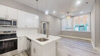 Located at 225 Park Ave in Baltimore's Mount Vernon neighborhood, this two-bedroom, one-bathroom unit offers a thoughtfully designed single-floor layout with modern finishes throughout. The open-concept kitchen serves as the heart of the home, showcasing white shaker cabinetry, a white quartz peninsula with an integrated sink, subway tile backsplash, and a full suite of stainless steel appliances including a French door refrigerator, electric range, and microwave. Pendant lighting above the island adds a contemporary touch, while light wood-style luxury vinyl plank flooring runs consistently through the entire space, creating a clean, cohesive aesthetic. The hallway connects the living area to both bedrooms and the bathroom. The primary bedroom is a comfortable, well-proportioned room featuring a ceiling fan, neutral gray walls, and ample closet space with double doors. The second bedroom benefits from a large street-facing window that fills the room with natural light and offers views of the surrounding urban neighborhood. The full bathroom is finished with white subway tile in the walk-in shower, a sliding glass door with brushed nickel hardware, and clean, minimalist fixtures. Throughout the unit, neutral gray walls and crisp white trim contribute to a bright, modern ambiance ideal for urban living.