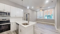 Located at 225 Park Ave in Baltimore's Mount Vernon neighborhood, this two-bedroom, one-bathroom unit offers a thoughtfully designed single-floor layout with modern finishes throughout. The open-concept kitchen serves as the heart of the home, showcasing white shaker cabinetry, a white quartz peninsula with an integrated sink, subway tile backsplash, and a full suite of stainless steel appliances including a French door refrigerator, electric range, and microwave. Pendant lighting above the island adds a contemporary touch, while light wood-style luxury vinyl plank flooring runs consistently through the entire space, creating a clean, cohesive aesthetic. The hallway connects the living area to both bedrooms and the bathroom. The primary bedroom is a comfortable, well-proportioned room featuring a ceiling fan, neutral gray walls, and ample closet space with double doors. The second bedroom benefits from a large street-facing window that fills the room with natural light and offers views of the surrounding urban neighborhood. The full bathroom is finished with white subway tile in the walk-in shower, a sliding glass door with brushed nickel hardware, and clean, minimalist fixtures. Throughout the unit, neutral gray walls and crisp white trim contribute to a bright, modern ambiance ideal for urban living.