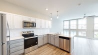 Located at 651 Meeting Street in Charleston, South Carolina, this single-floor unit sits within the city's dynamic Upper Peninsula neighborhood. The open-concept layout creates a seamless flow between the kitchen and living areas, making the space feel bright and expansive.

The kitchen is a standout feature, designed with a two-tone cabinet scheme pairing crisp white upper cabinets with soft gray lower cabinets, all accented by brushed nickel hardware. A classic white subway tile backsplash adds texture, while light quartz countertops provide ample workspace. The peninsula extends the counter space and subtly defines the boundary between kitchen and living area. A full suite of stainless steel appliances—including a Whirlpool range, over-the-range microwave, dishwasher, and refrigerator—completes the kitchen. Pendant lighting adds a modern, refined touch overhead.

The living area is generously proportioned, featuring light wood-look flooring that runs throughout the unit, a ceiling fan, and floor-to-ceiling windows that flood the space with natural light and offer views of the surrounding greenery.

The bathroom maintains the unit's clean aesthetic, with white subway tile surrounding the soaking tub and shower combination, complemented by wood-look flooring that ties cohesively to the rest of the unit. Overall, the space presents a contemporary, well-appointed design ideal for modern urban living.