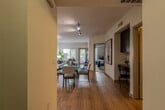 This single-floor residence offers a thoughtfully designed layout that seamlessly connects the living, dining, and kitchen areas. Warm hardwood-style flooring runs throughout the main living spaces, complemented by neutral walls and an abundance of natural light streaming in through large windows with horizontal blinds. A glass-panel door provides direct outdoor access from the living room, enhancing the bright and airy atmosphere.

The living area is generously proportioned, featuring track lighting and room for comfortable seating arrangements. Adjacent to it, the dining space accommodates a glass-top table and chairs, creating a natural transition between the kitchen and living room. The kitchen is well-equipped with dark espresso cabinetry, granite-style countertops, stainless steel appliances including a refrigerator, range, microwave, and dishwasher, all set atop matching hardwood-style flooring.

The bedroom offers a tranquil retreat with plush carpeting, a window with garden views, and direct access to a spacious walk-in closet complete with full-length hanging rods and open shelving. The bathroom features a dark-cabineted vanity with a white countertop, open wall shelving, and a full shower-tub combination, maintaining the unit's clean and functional aesthetic throughout.