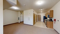 Located at 305 Fifth Ave S in Saint Cloud, Minnesota, this single-floor unit offers a practical and well-organized layout designed for efficient everyday living. The kitchen serves as a functional centerpiece, featuring a full lineup of black appliances — including a refrigerator, electric range, and over-the-range microwave — set against dark countertops and framed by warm oak cabinetry that extends to the upper walls for generous storage. Light vinyl flooring runs throughout the kitchen and entryway, providing a clean and durable surface. A dedicated entryway with a secure door and adjacent closet space adds convenience and organization upon arrival. The open living area is carpeted and bathed in neutral tones, creating a calm and versatile space that can be arranged to suit various needs. A textured ceiling and flush-mount lighting are consistent throughout, contributing to a cohesive interior aesthetic. The bathroom includes an oak vanity with a white countertop and under-sink cabinetry, a large mirror with overhead lighting, and a medicine cabinet for additional storage. Overall, the unit presents a straightforward and functional design with consistent warm wood finishes, making it a practical living space in a convenient Saint Cloud location.