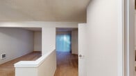 This two-story residence offers a well-organized layout spread across two levels, connected by a staircase visible in the floor plan. The main level features a kitchen equipped with white cabinetry, granite-style countertops, a full suite of white appliances including a refrigerator, electric range, and dishwasher, all set atop warm hardwood-style flooring. A peninsula counter with bar-height seating creates an open connection to the adjacent living area, which is finished with plush carpeting and a sliding glass door fitted with vertical blinds that invites natural light and provides access to an outdoor area. A convenient half-bath and in-unit washer and dryer are also located on this level, with upper cabinetry providing added storage in the laundry space. The upper floor hosts the bedrooms, each featuring ceiling fans with integrated lighting, soft carpet flooring, and windows dressed with vertical blinds. The primary bedroom includes a spacious walk-in closet with built-in shelving and rod, as well as access to a private bathroom. A second bedroom also benefits from multiple windows. Textured ceilings and baseboard heating are consistent throughout, contributing to the home's practical, comfortable character.