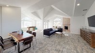 Located at 5301 S Bannock St in Littleton, Colorado, this single-floor community clubhouse is designed to accommodate a variety of social and functional needs. The space is characterized by soaring vaulted ceilings, crisp white walls, and an abundance of natural light streaming through multiple arched and standard windows, creating an open and airy atmosphere throughout.

The main gathering area serves as the heart of the clubhouse, featuring patterned blue-toned carpeting, modern sectional seating, and a wall-mounted television. A striking brick fireplace anchors one end of this room, complemented by additional lounge seating and side tables. Arched windows frame natural views and contribute to the architectural character of the space.

An open business center nook accommodates multiple workstations with built-in desks, ergonomic seating, and computer equipment, lit generously by natural light. A quieter lounge nook with curated accent chairs provides a more intimate setting for relaxed conversation or reflection.

The game area includes a foosball table and colorful casual seating, offering a lively recreational option. The full kitchen is outfitted with white shaker cabinetry, white countertops, stainless steel appliances, and light wood-look flooring. A dedicated dining area rounds out the amenities, making this a well-appointed and versatile community facility.