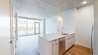 Located on the 11th floor at 333 E Superior St in Duluth, Minnesota, this contemporary one-bedroom, one-bathroom unit offers a refined urban living experience with striking architectural character. Exposed concrete ceilings throughout lend an industrial-chic aesthetic, complemented by warm wood-tone luxury vinyl plank flooring that flows seamlessly across every room.

The open-concept kitchen and living area form the heart of the unit. The kitchen features white flat-front cabinetry, a crisp white quartz peninsula with an undermount sink, white subway tile backsplash, and a full suite of stainless steel appliances including a range, microwave, dishwasher, and French door refrigerator. The adjoining living area is bright and spacious, anchored by floor-to-ceiling sliding glass doors that open to a private balcony with sweeping views of Lake Superior and the Duluth cityscape.

The generously sized bedroom continues the exposed concrete ceiling design and benefits from its own set of large windows framing the same stunning lake views. A dedicated walk-in closet with wire shelving provides practical storage. The bathroom is finished in a clean, modern palette with white tile surround for the tub/shower combo, a floating vanity with backlit mirror, and warm wood-tone flooring that ties the space together cohesively.
